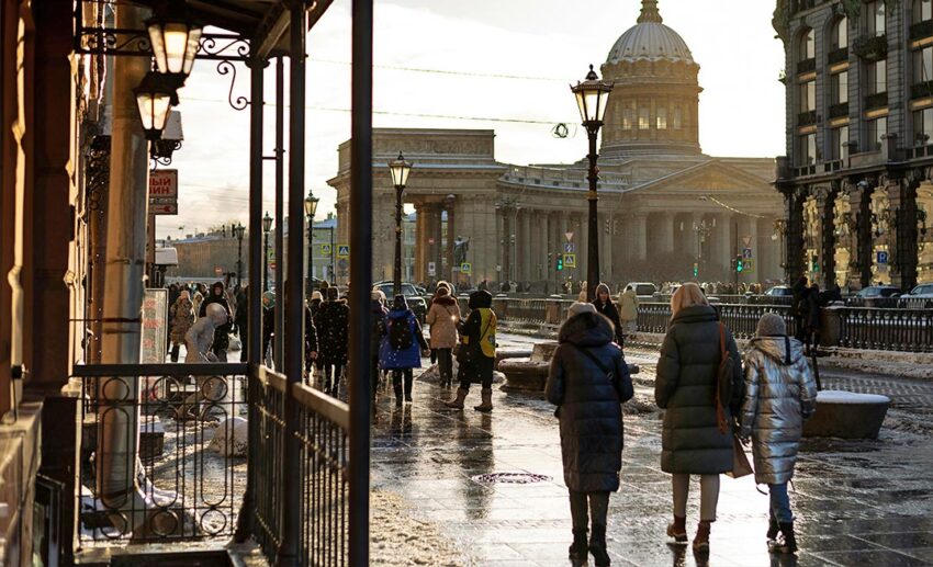 Pedestrians walking down a sunny, wide European sidewalk lined with grand, historic architecture in Saint Petersburg, Russia.