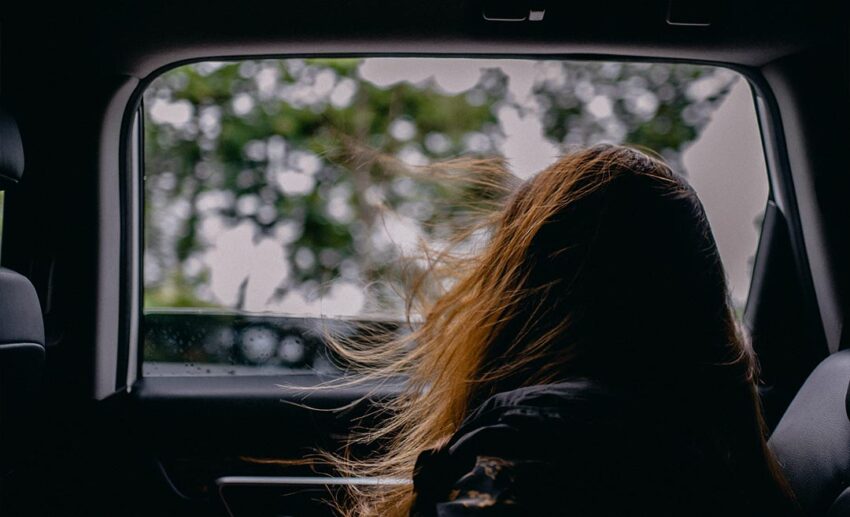 Back view of a woman driving or sitting inside a car looking at the road ahead during an extended road trip for burnout recovery.