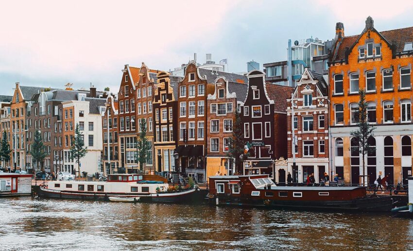 Traditional houseboats and canal boats moored along a scenic historic waterway lined with classic brick buildings in Amsterdam, Netherlands.