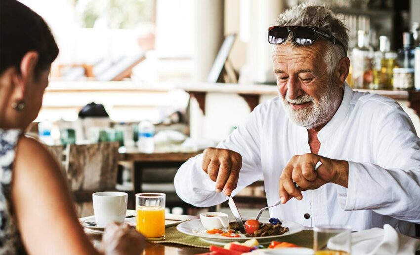 Senior father eating a local hotel breakfast across from his adult daughter during a multigenerational culinary trip