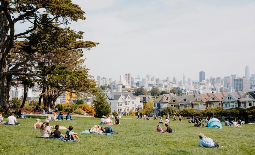 Residents and travellers relaxing on the grass of an urban public park overlooking a beautiful city skyline at sunset.