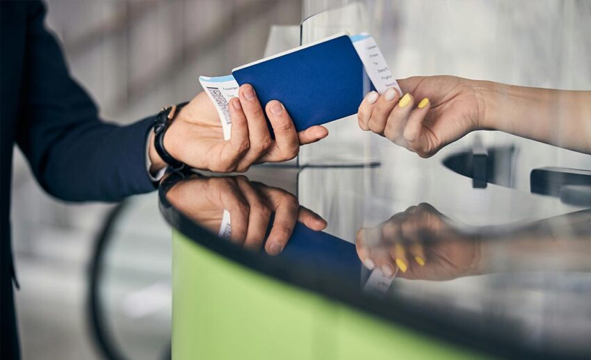 A close-up shot of an international traveller's hands handing a passport booklet and airline boarding passes to an airport staff member.