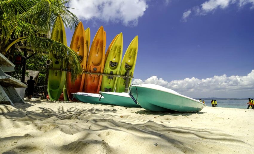 Brightly coloured canoe boats resting on the powdery white sand beach of Kapas Island, Terengganu, a tranquil tropical paradise for burnout recovery.