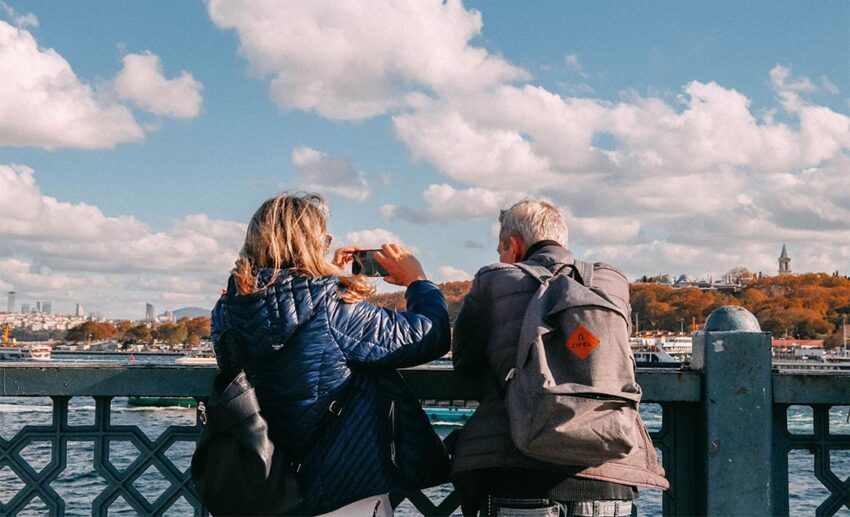 Two adults enjoying a scenic river view from a bridge under a vibrant sunset sky during a planned family travel journey