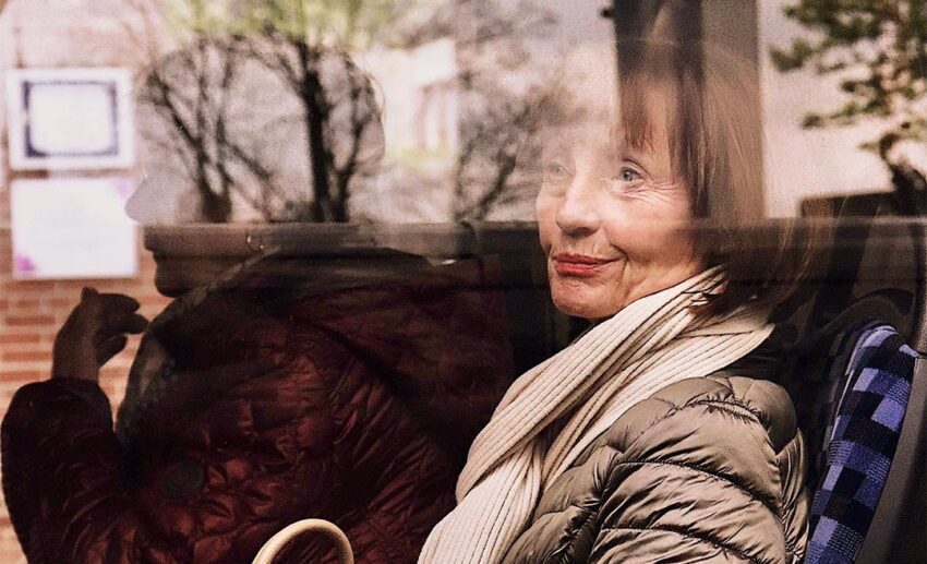A mature female traveller sitting by a window on public transit, looking thoughtfully at the city street reflections outside.