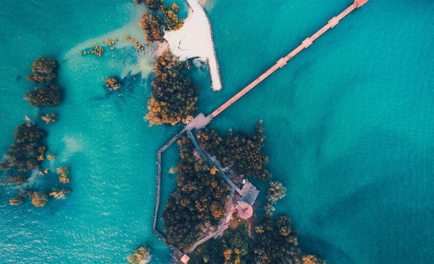 An aerial drone view of a small green island surrounded by calm ocean waters off the coastline of Port Dickson, Negeri Sembilan.
