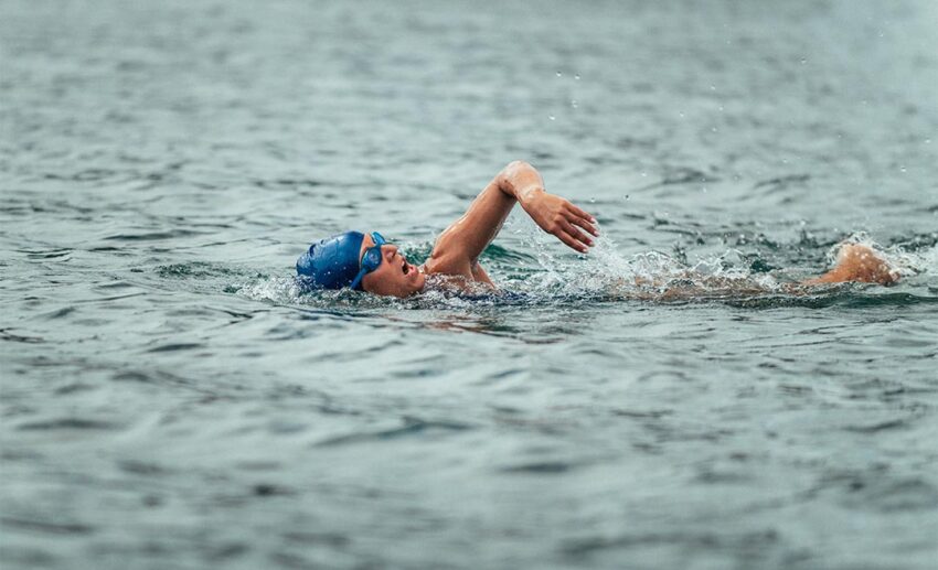 A top-down view of a solo woman swimming systematically through deep blue seawater, creating ripples.
