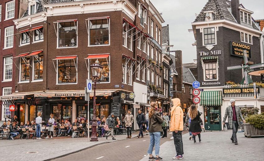 Pedestrians and solo female travellers walking safely down a clean, well-lit urban street lined with tall buildings in Amsterdam, Netherlands.