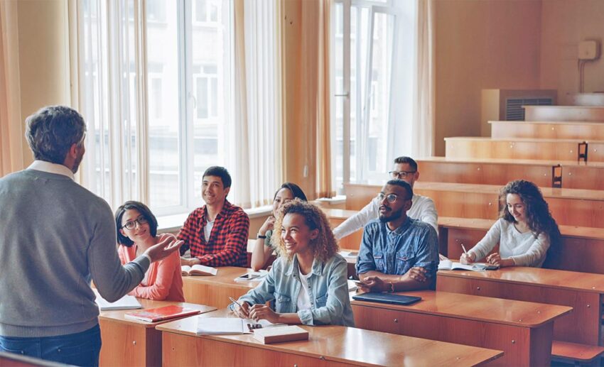 A group of young international students engaged in a lively conversation with an educational instructor inside a bright university setting.