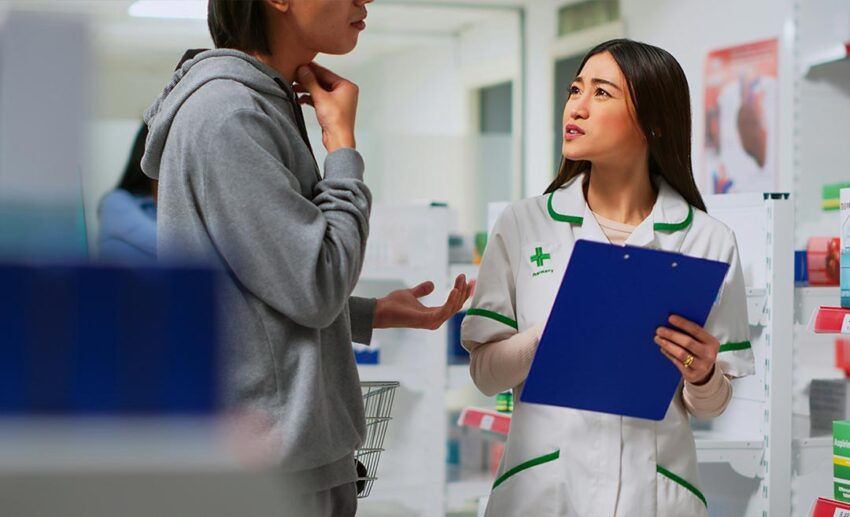 A customer speaking with a female pharmacist about medication inside a local community pharmacy to evaluate healthcare access.