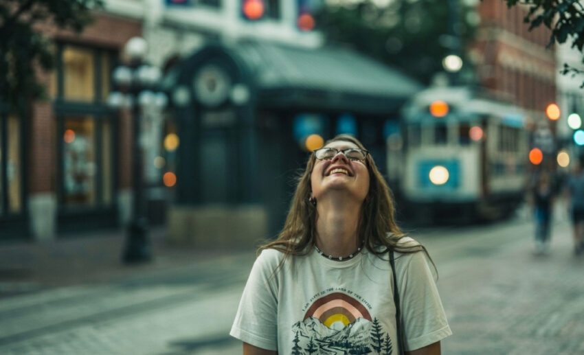 A relaxed independent woman standing on a peaceful street corner with her eyes closed, smiling up at the warm sunlight.