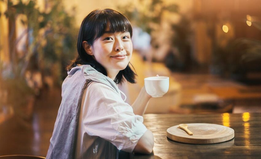 A relaxed female traveller enjoying a hot cup of coffee in a warm, cosy local cafe during a slow travel trip.