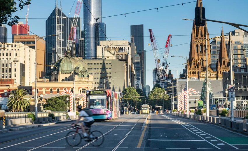 A classic city tram driving down Melbourne's St Kilda Road past a cyclist during an early morning commute.