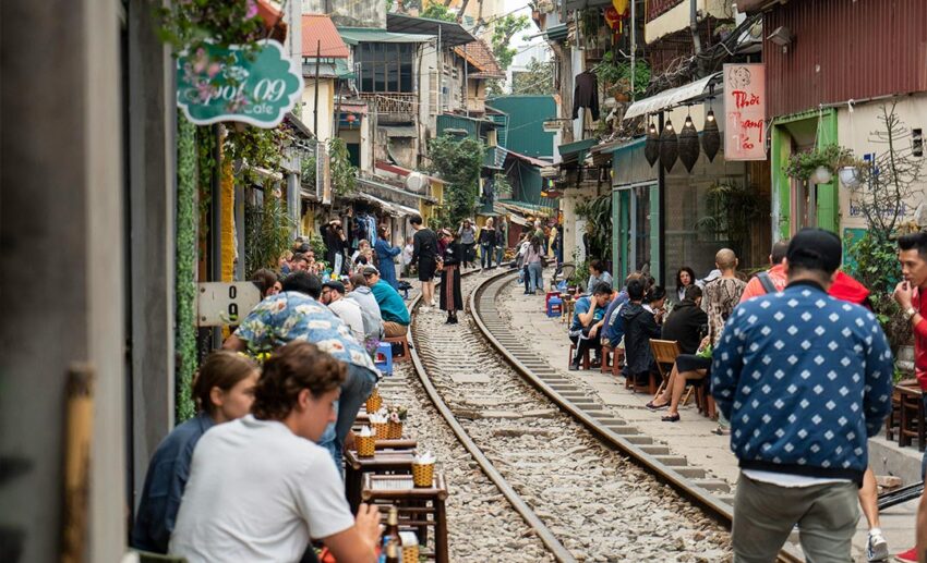 Domestic and international travellers walking along the narrow tracks of Hanoi Train Street lined with cafes and historic buildings in Hoan Kiem, Vietnam.