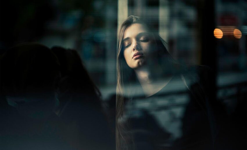 A fatigued female passenger leaning her head against a glass transport window with her eyes closed, looking exhausted.