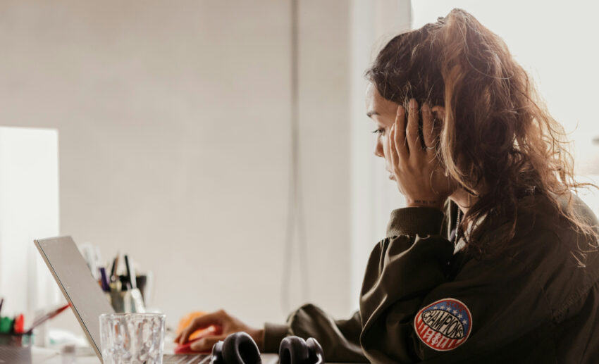A professional woman sitting at her office desk looking contemplative and bored, thinking about how to plan a career break.
