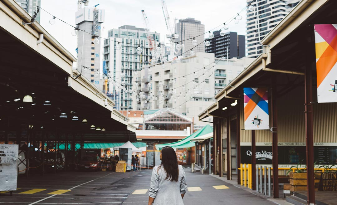 A woman standing confidently on a street between residential buildings in a foreign city during a relocation trial.