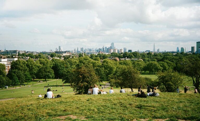 Groups of people sitting on a lush green grass hill in London UK enjoying a sunny afternoon.