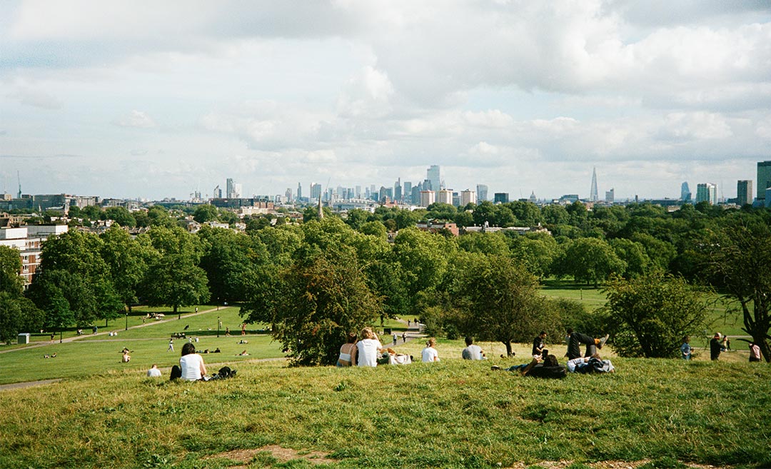 Groups of people sitting on a lush green grass hill in London UK enjoying a sunny afternoon.