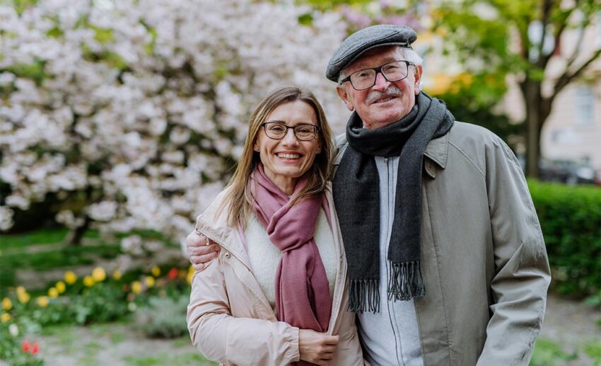 Adult daughter hugging her senior father outdoors in a park during a father daughter travel trip.