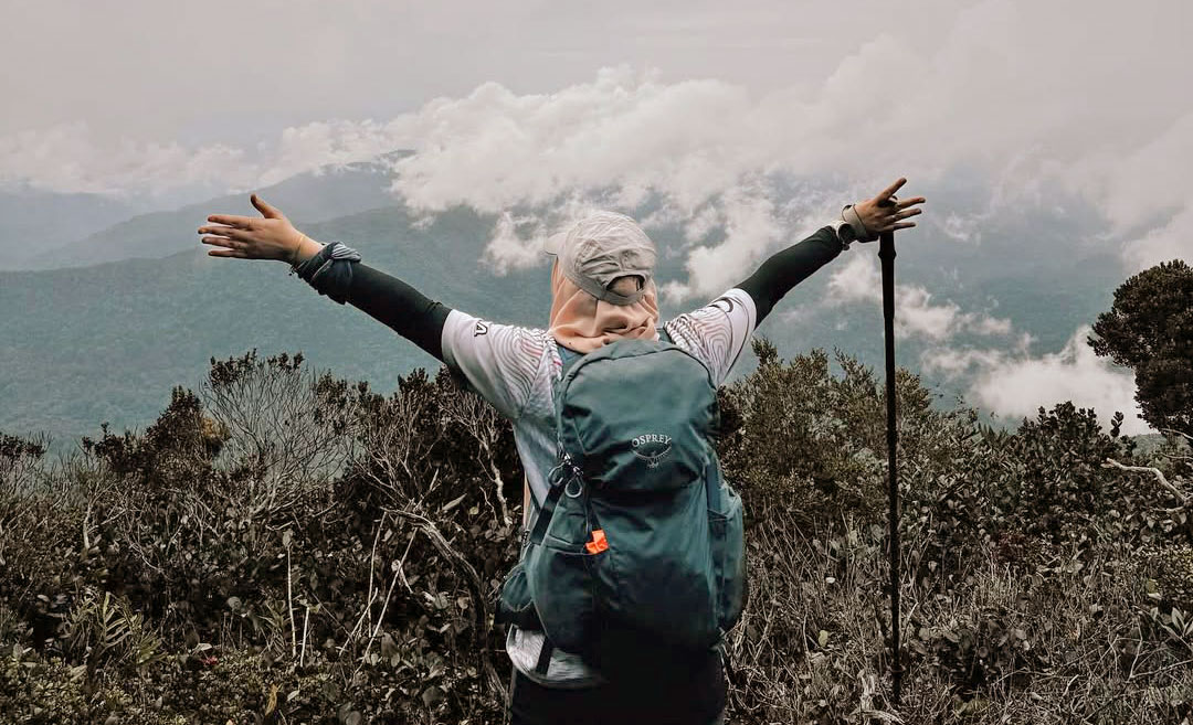 Malaysian female hiker with arms raised at the peak of Gunung Yong Yap overlooking dense rainforest mountain trails