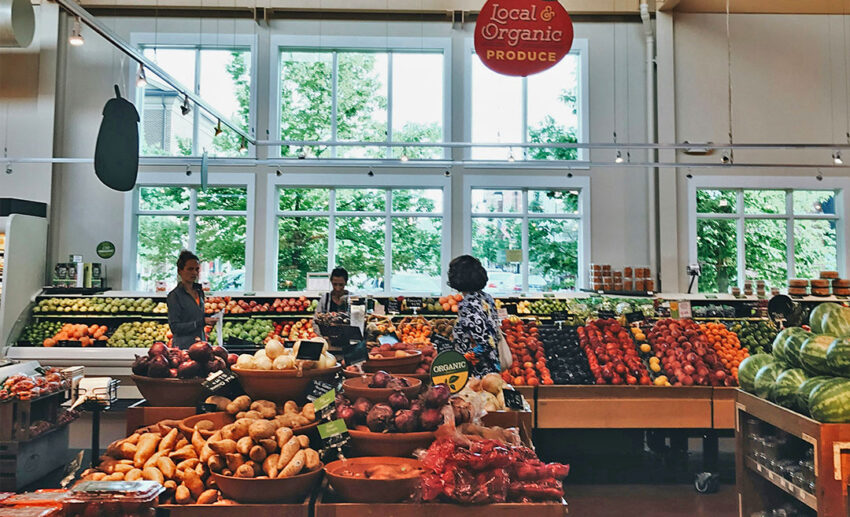 Shoppers on daily errands inspecting fresh produce and fruits in the brightly lit aisles of a local grocery store.
