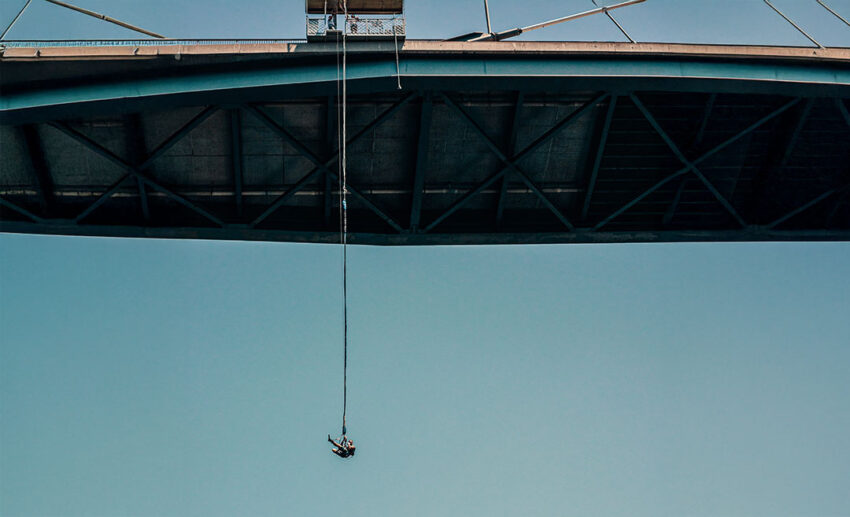 A distant view of a person bungee jumping from the high, cable-stayed Franjo Tudjman Bridge in Dubrovnik, Croatia, suspended over the blue Adriatic Sea.