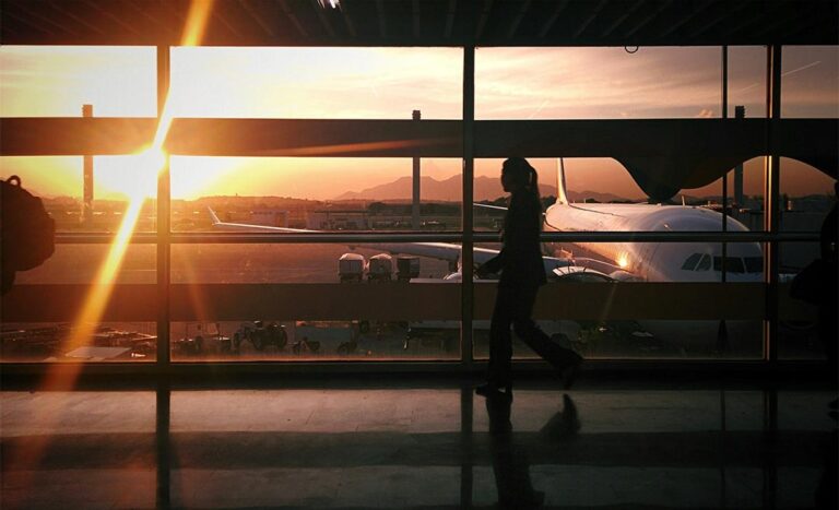 Silhouette of a woman carrying luggage past a large airport window looking out at an airplane, illustrating taking a career break to travel.