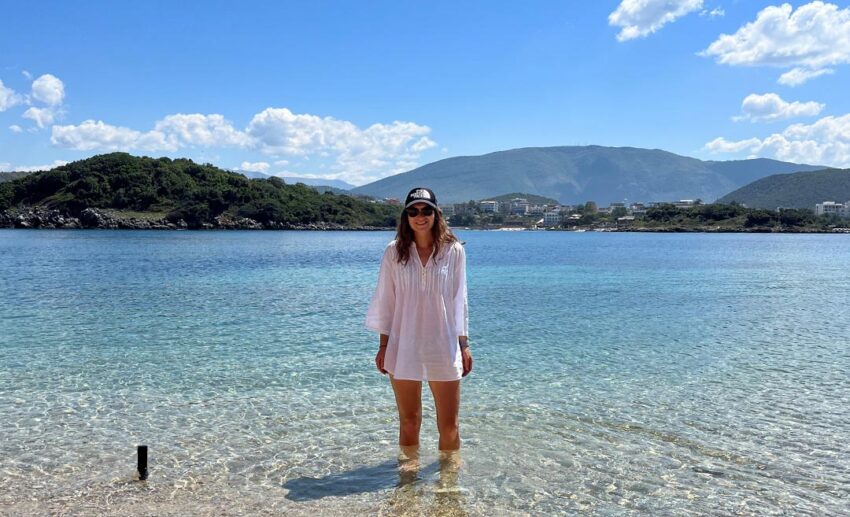 A solo female traveller standing ankle deep in the crystal clear turquoise sea water in Ksamil, Albania, practicing a slow travel lifestyle design.