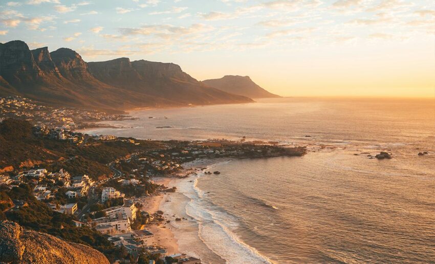 A beautiful sunset view over rugged rocky mountains meeting the sea along the coastline of Cape Town, South Africa.