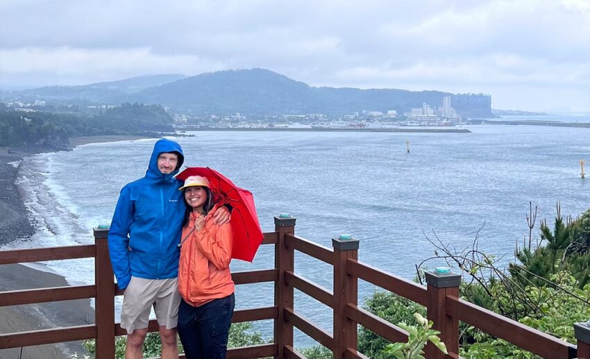 Sofia and her travel companion posing together along the rugged rock formations of the Yeongmeori coastal path leading towards Sanbanggulsa Temple.