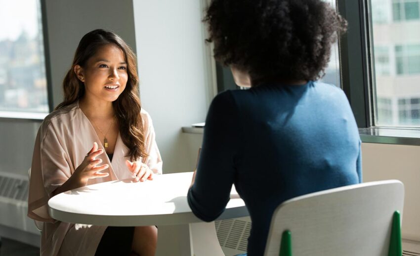 Two professional women sitting face to face having a conversation, explaining how to handle a career gap on a CV.