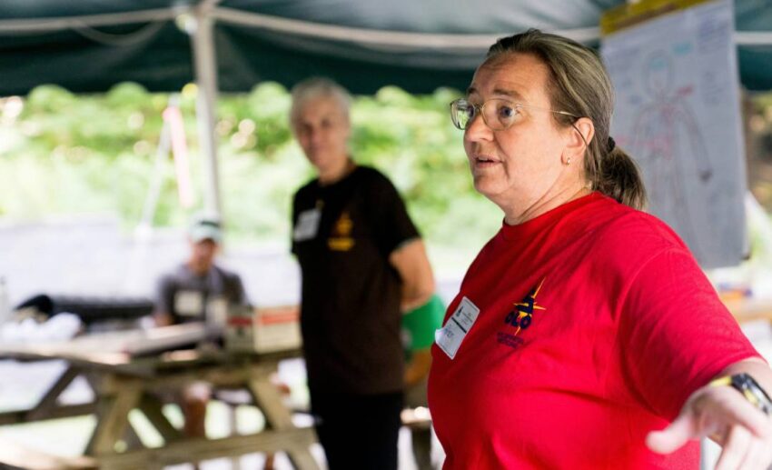 A woman in a red shirt leading an engaging discussion with an attentive group outdoors