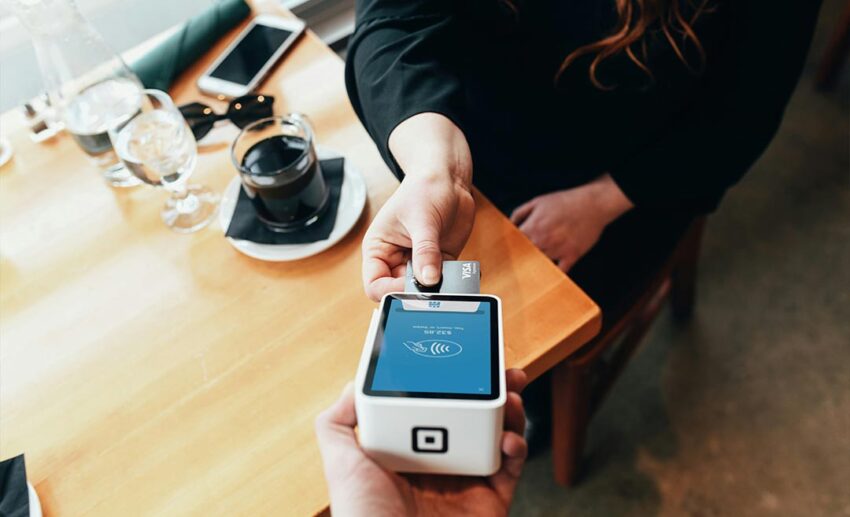 Close-up of a person holding a contactless credit card terminal swipe machine, focusing on maximizing travel rewards, points, and air miles through daily transactions.