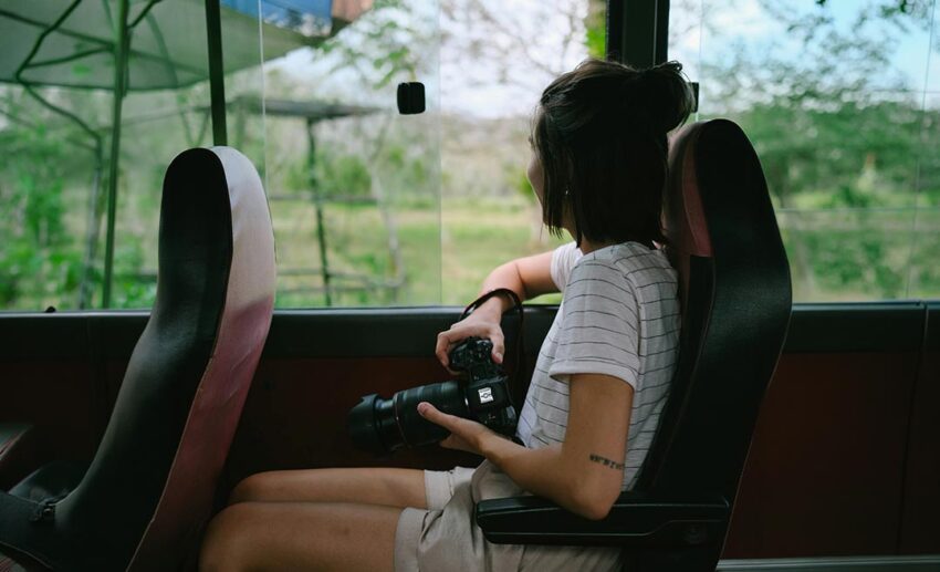 A woman sitting by a bus window holding a camera and gazing at the passing scenery
