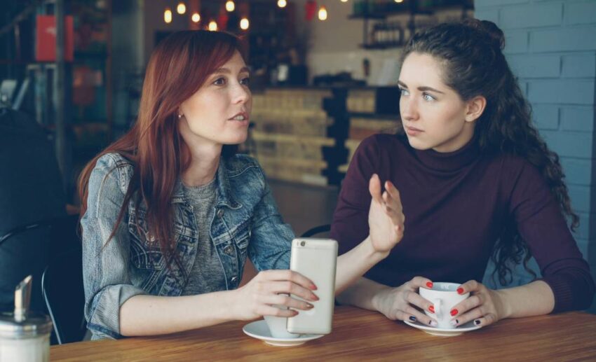 Two women sitting together at a wooden cafe table having an earnest conversation over drinks