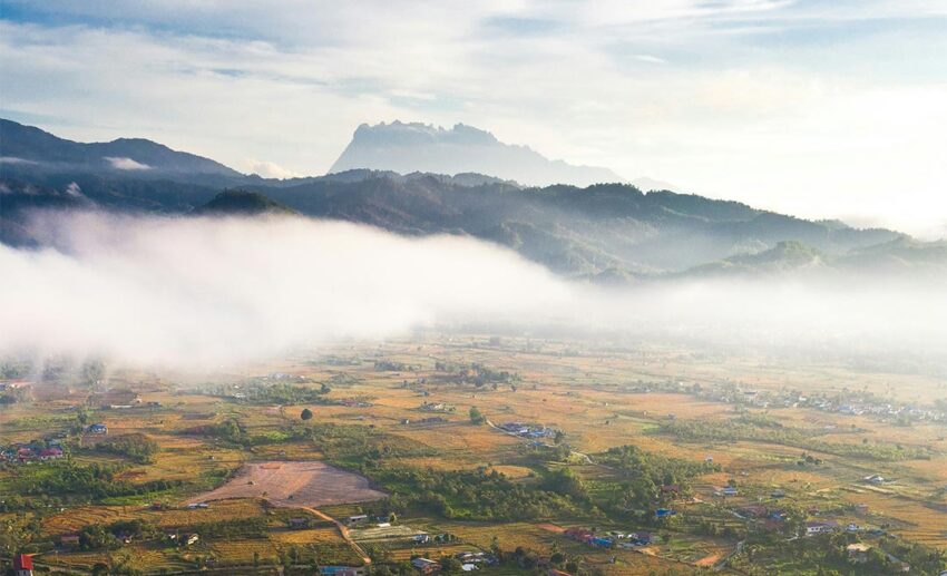 Aerial view of a quiet village surrounded by lush mountains and forested hills in Tambunan, Sabah