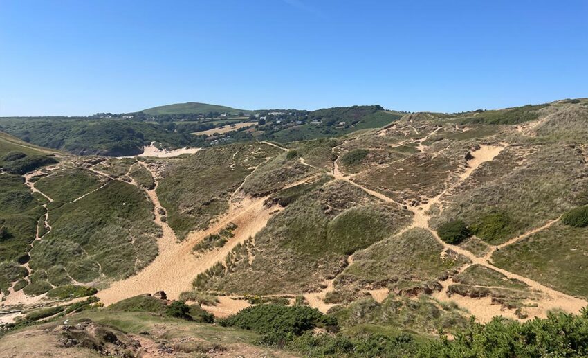 Grassy green cliffs and rolling dunes sloping smoothly down to the sandy shore of Pobbles Bay