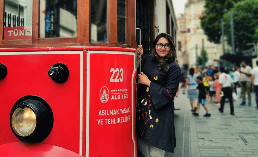 A woman posing happily alongside a historic red tram on a street in Istanbul