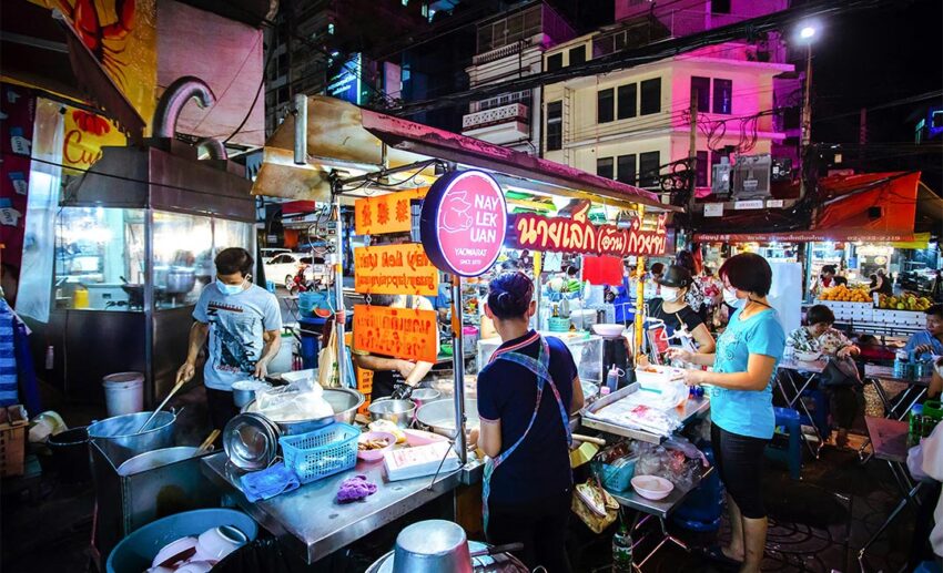 Street food vendors at the famed Nay Lek Uan stall in Bangkok Chinatown serving rolled noodle soup with crispy pork
