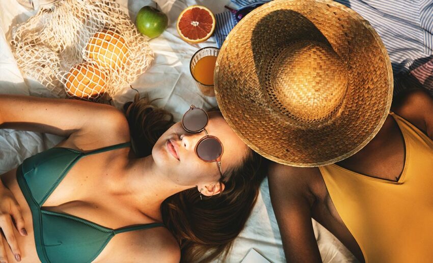 Two cheerful young Asian women in swimsuits sun tanning together on a beach holiday, learning how to rest.