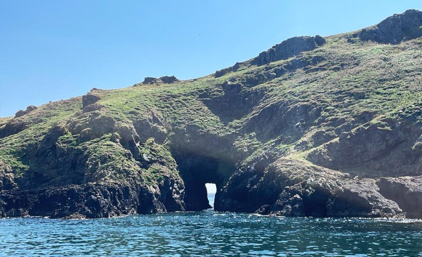 Rocky cliffs of Skomer Island viewed from the sea, showing a narrow natural sea tunnel carved through the stone
