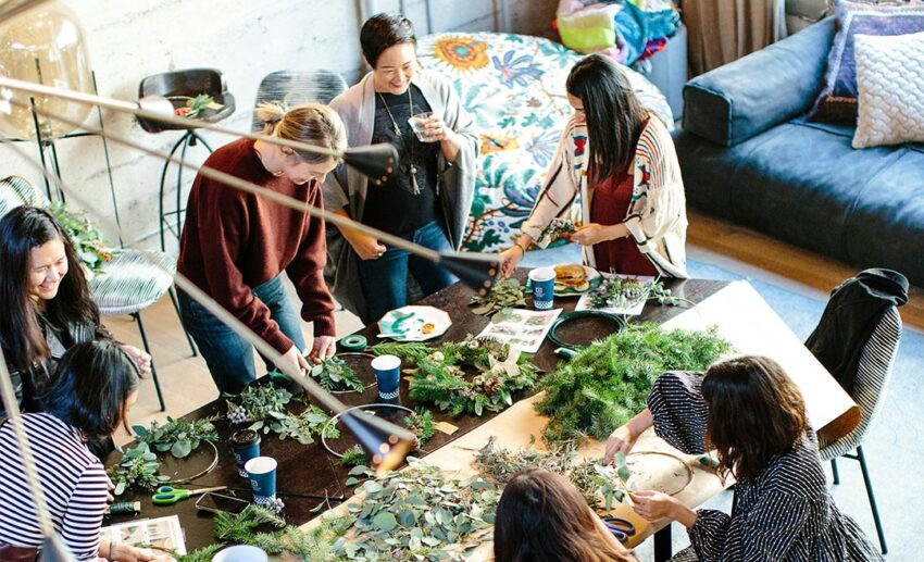A group of women gathered around a wooden workbench participating in an intimate botanical workshop