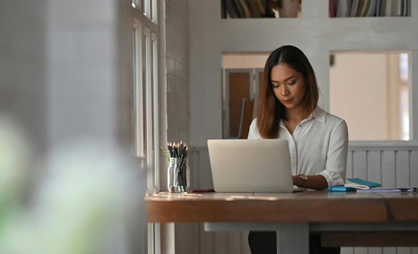 A businesswoman sitting at her laptop in a home office, experiencing burnout from intense corporate culture.