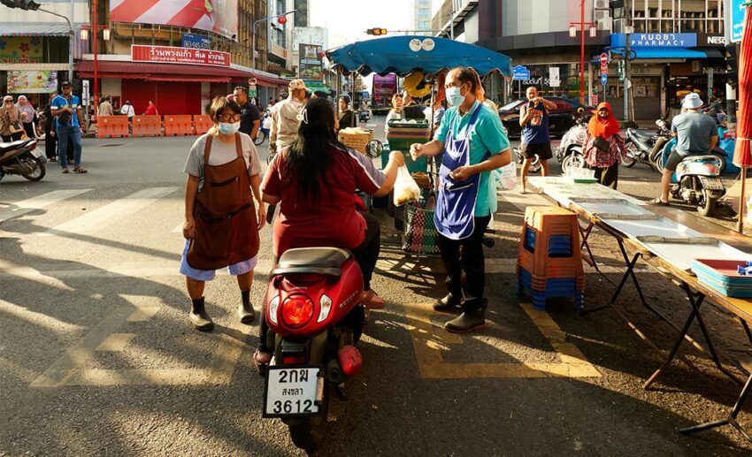 A woman on a motorbike purchasing fresh goods from a street vendor at an authentic morning market in Hat Yai, Songkhla, Thailand.