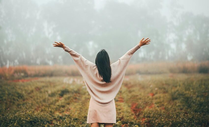 Rear view of a woman standing with open arms in a misty forest enjoying nature