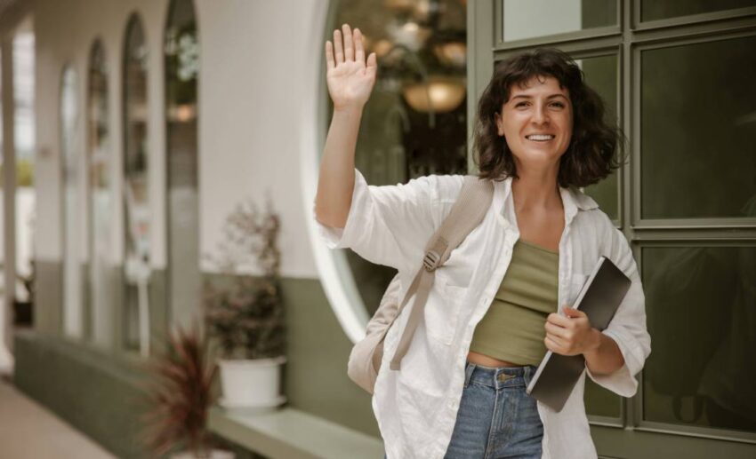 A woman smiling while raising her hand and waving goodbye