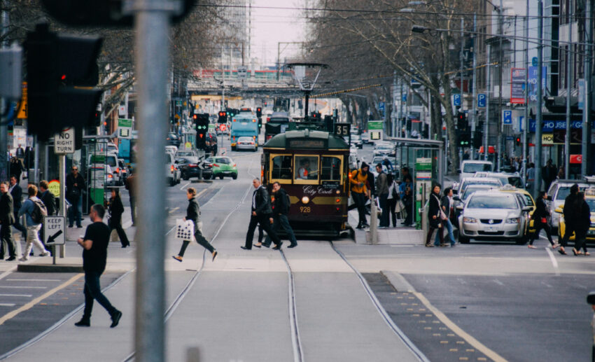 Pedestrians crossing a city street next to a classic yellow tram in Melbourne, exploring different urban neighbourhoods.