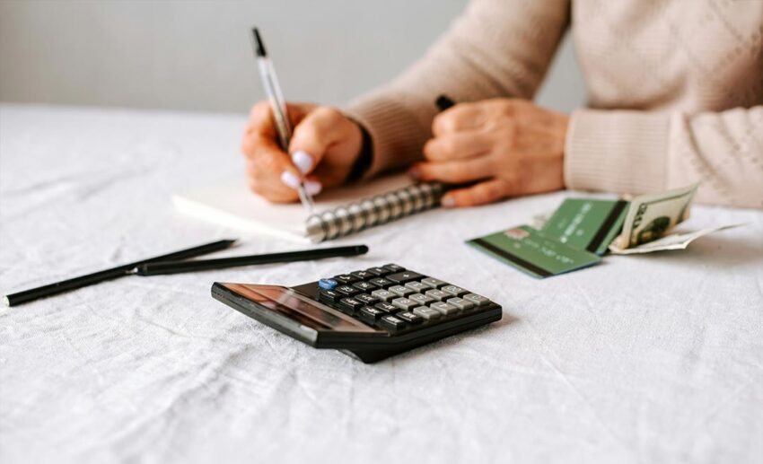 A close-up shot of a professional mapping out a career transition strategy, writing action steps in a paper notebook next to an office calculator.