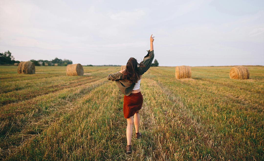 A cheerful woman tossing her hat in the air in a field during evening golden hour